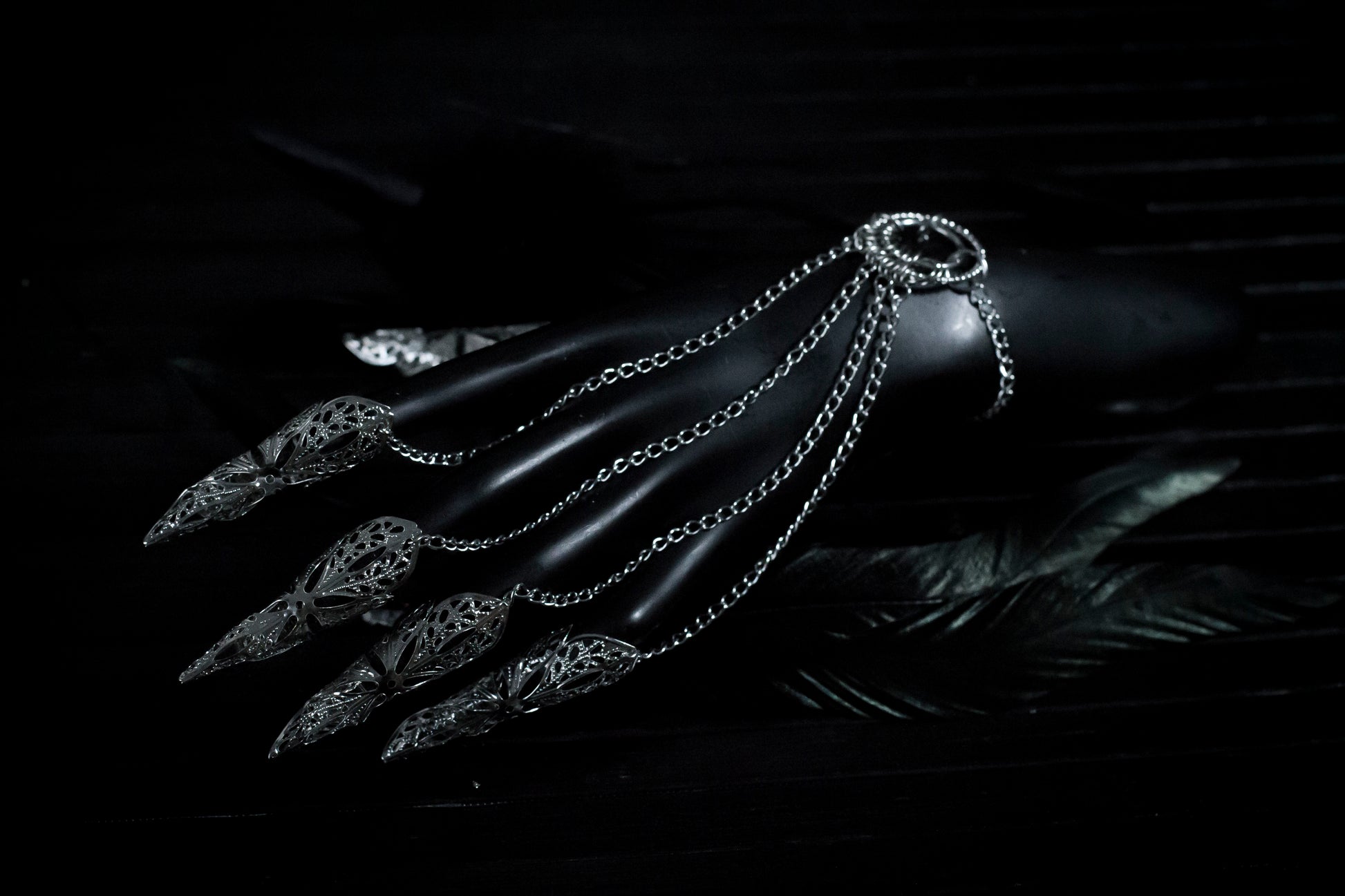 A close up shoot of a hand that extends dramatically with Myril Jewels' hand chain bracelet, each finger tipped with a delicate claw ring. The jewelry's silver filigree work captures the dark, neo-gothic aesthetic, perfect for adding a bold touch to Halloween looks or as a statement piece for those who favor gothic-chic or witchcore styles.