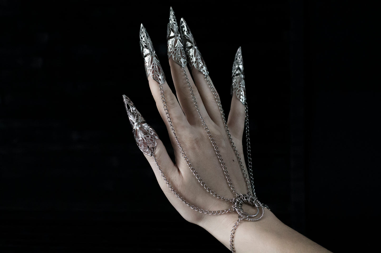 A hand adorned with Myril Jewels' hand chain bracelet with silver claws, reflecting a darkly opulent neo-goth style. This captivating piece is perfect for those who favor gothic-chic jewelry, making it an ideal choice for witchcore looks, rave parties, or as a daring gift for the bold at heart.