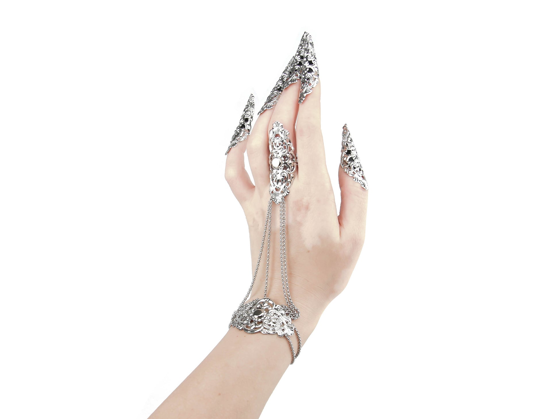 A stunning silver hand chain adornment with a gothic-inspired design is shown off on a hand adorned with sharp nail claws, capturing the essence of goth fashion. The piece boasts intricate filigree metalwork that adorns the back of the hand, while chains elegantly connect the bracelet portion to the middle finger ring. The background is a crisp white, emphasizing the refined and mysterious charm of this meticulously crafted creation.