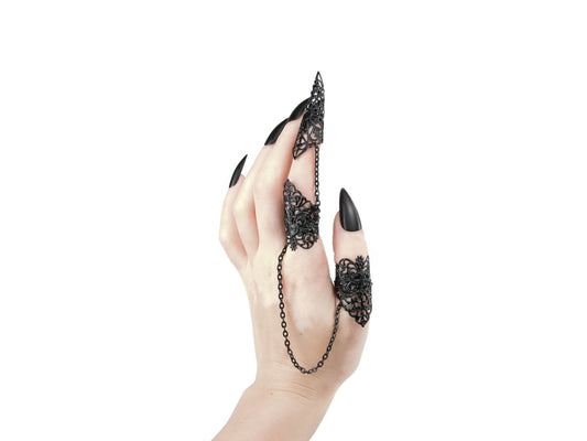 A hand showcases a unique Myril Jewels gothic black double ring, extending into nail claws for a striking look. This piece captures the neo-gothic essence, blending witchcore and whimsigoth influences, ideal for those embracing a dark, avant-garde aesthetic in their everyday wear or as a statement piece for festivals and rave parties.
