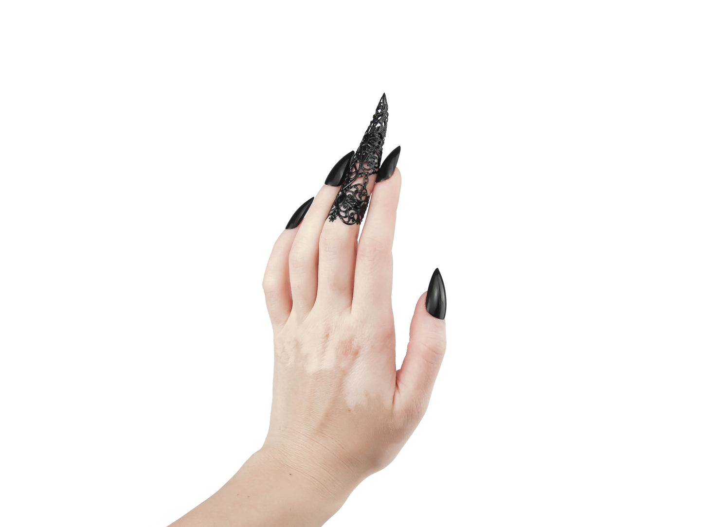A hand adorned with a Myril Jewels claw ring on the middle finger commands attention in this image, perfect for those with a passion for dark-avantgarde and neo-goth aesthetics. The ring's black, lace-like filigree design extends into a sharp, claw-like point, encapsulating the essence of gothic-chic jewellery. This bold piece is ideal for Halloween, embodying the witchcore trend with a touch of whimsigoth flair. The ring's dramatic style makes it a captivating accessory for everyday wear