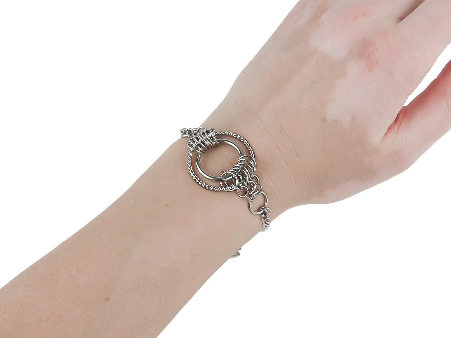 An intricate Myril Jewels chainmail-style bracelet adorns the wrist, featuring a prominent O-ring centerpiece. This silver-toned piece captures the essence of neo-goth fashion, merging dark-avantgarde with gothic-chic. It's an ideal accessory for those who embrace a witchcore or whimsigoth lifestyle, and a versatile addition to any Halloween, rave party, or festival jewel collection, reflecting a commitment to everyday wearable art for the alternative style lover.