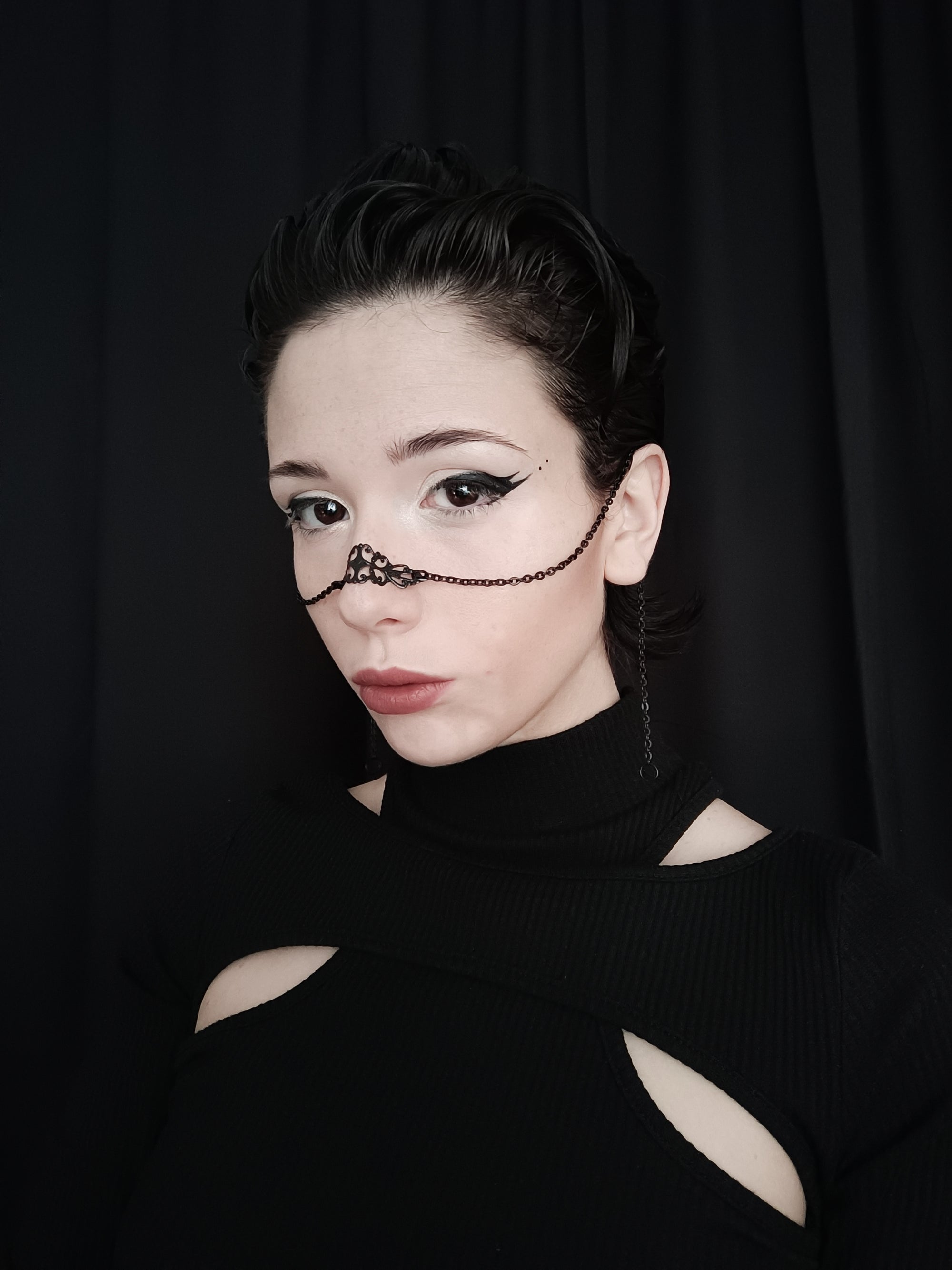 A model poses against a dark background, wearing a delicate Myril Jewels black nose chain with intricate filigree, embodying the essence of neo-gothic jewelry. This piece is a perfect addition to a gothic-chic wardrobe, suitable for everyday wear, and a unique gift idea for those who love bold, alternative styles.