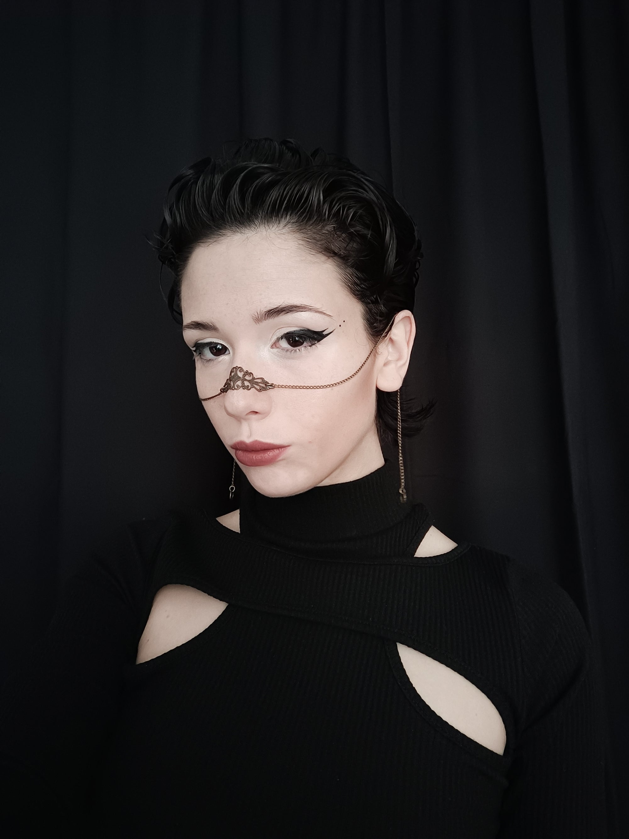 A model dons a Myril Jewels bronze nose chain against a dark backdrop, a perfect piece for those inspired by neo-gothic and whimsigoth fashion. It's a versatile accessory, ideal for adding a gothic-chic edge to everyday wear, or as a bold statement at rave parties and festivals.