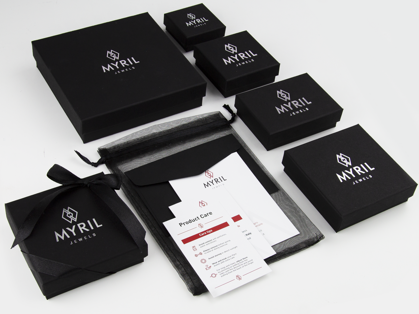 Assortment of Myril Jewels brand packaging, featuring elegant black boxes of various sizes with the company's logo in white, along with care instructions and black organza gift bags, representing sophisticated goth jewelry presentation and branding.
