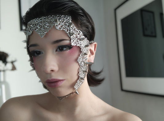 A model from Myril Jewels displays a punk filigree face frame mask embellished with studs, exuding a neo-gothic charm. This statement piece merges gothic-chic with bold punk influences, perfect for Halloween, festival wear, or adding an avant-garde edge to everyday goth style.