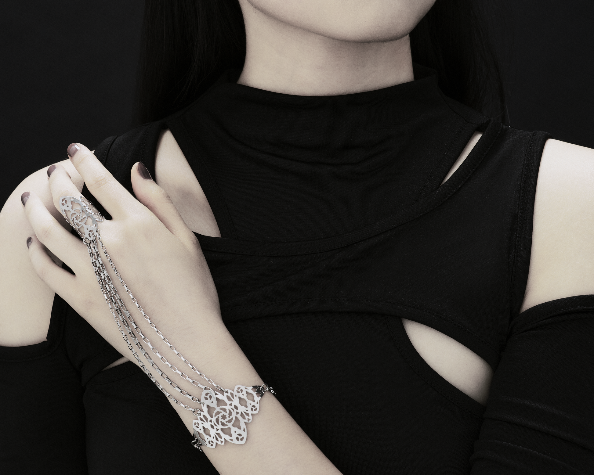 A poised hand adorned with a Myril Jewels hand chain graces the frame. Intricate filigree inspired by gothic arches drapes over the wrist, linking to a filigree ring, exemplifying the brand's fusion of dark elegance and architectural grace, perfect for the gothic-avantgarde enthusiast's collection.