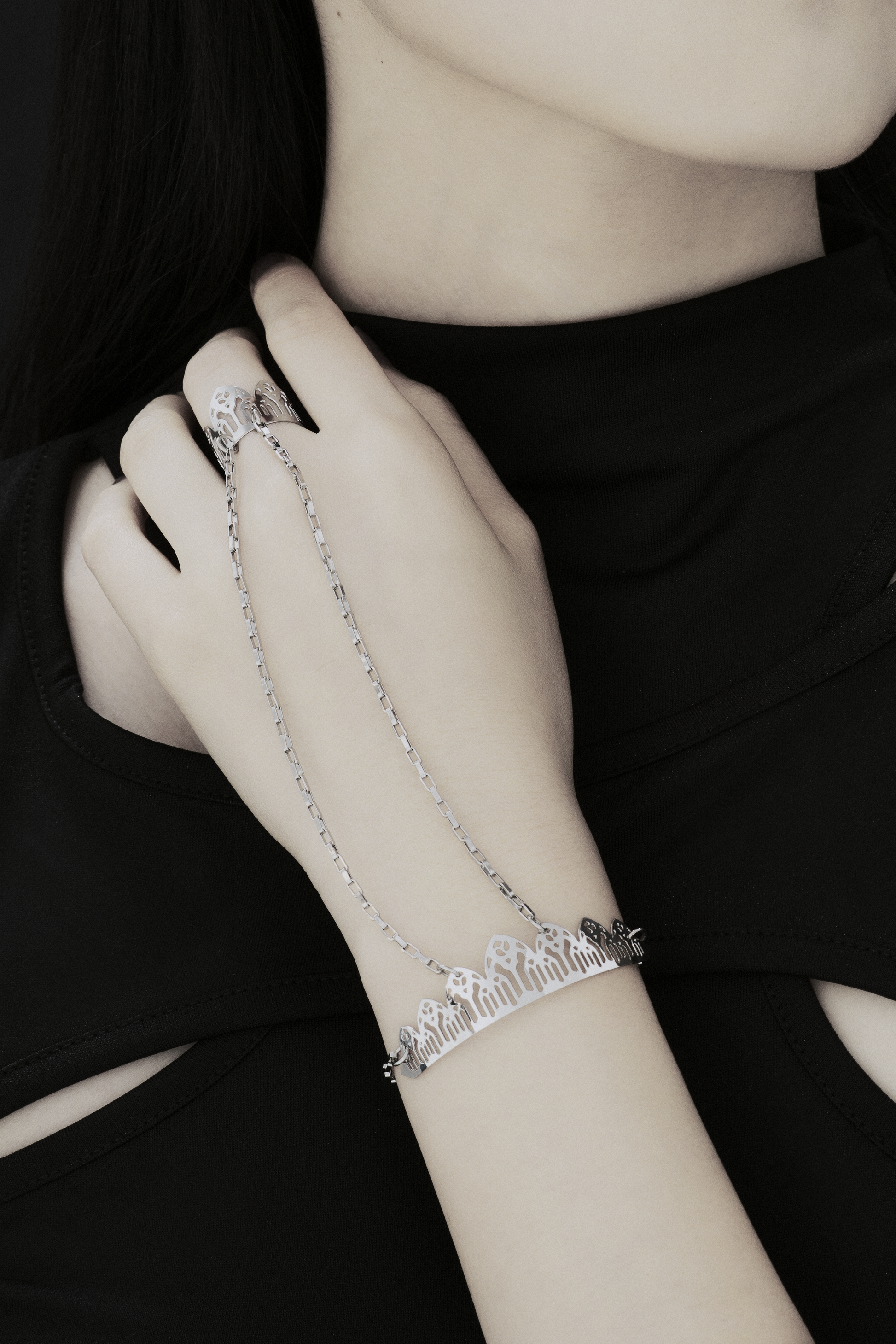 This Myril Jewels hand chain bracelet ring exudes gothic elegance, featuring a design inspired by the pointed arches of Gothic architecture. The bracelet encircles the wrist with a delicate yet bold chain, leading to a detailed ring that crowns the finger with a silhouette of arches, embodying the Neo-Gothic aesthetic. Crafted for the dark-avantgarde enthusiast, it's a versatile piece that complements both everyday minimal goth looks and elaborate festival or rave party outfits.