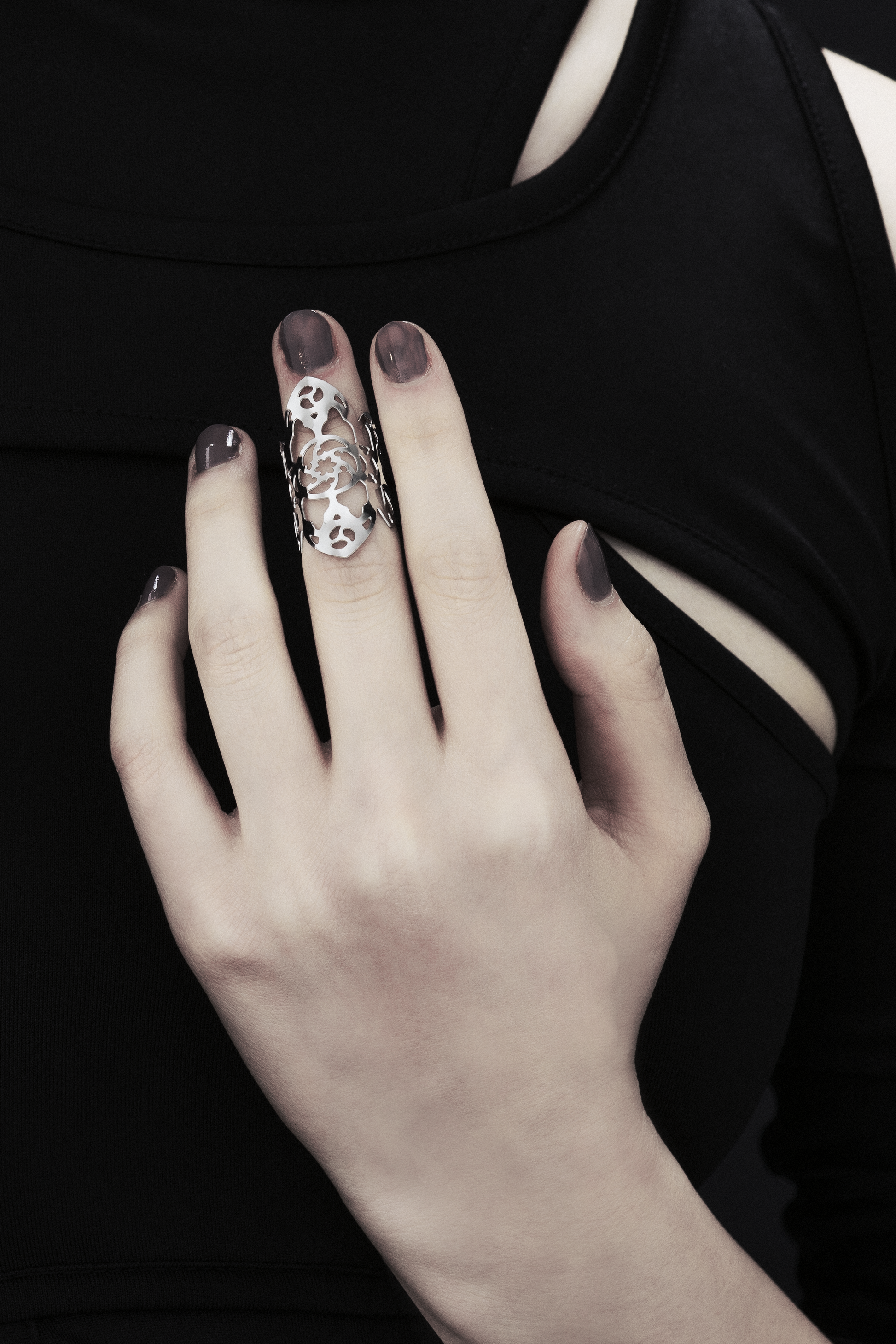 A model wears a Myril Jewels gothic architecture-inspired midi ring on her middle finger, complementing her dark manicure and black, cut-out shoulder top. The ring's intricate design and silver finish echo the sophisticated, dark-avantgarde style, perfect for fans of neo-gothic and gothic-chic jewelry. This piece blends seamlessly with a witchcore aesthetic, making it suitable for Halloween, everyday wear, and as a distinctive accessory for rave parties and festivals.