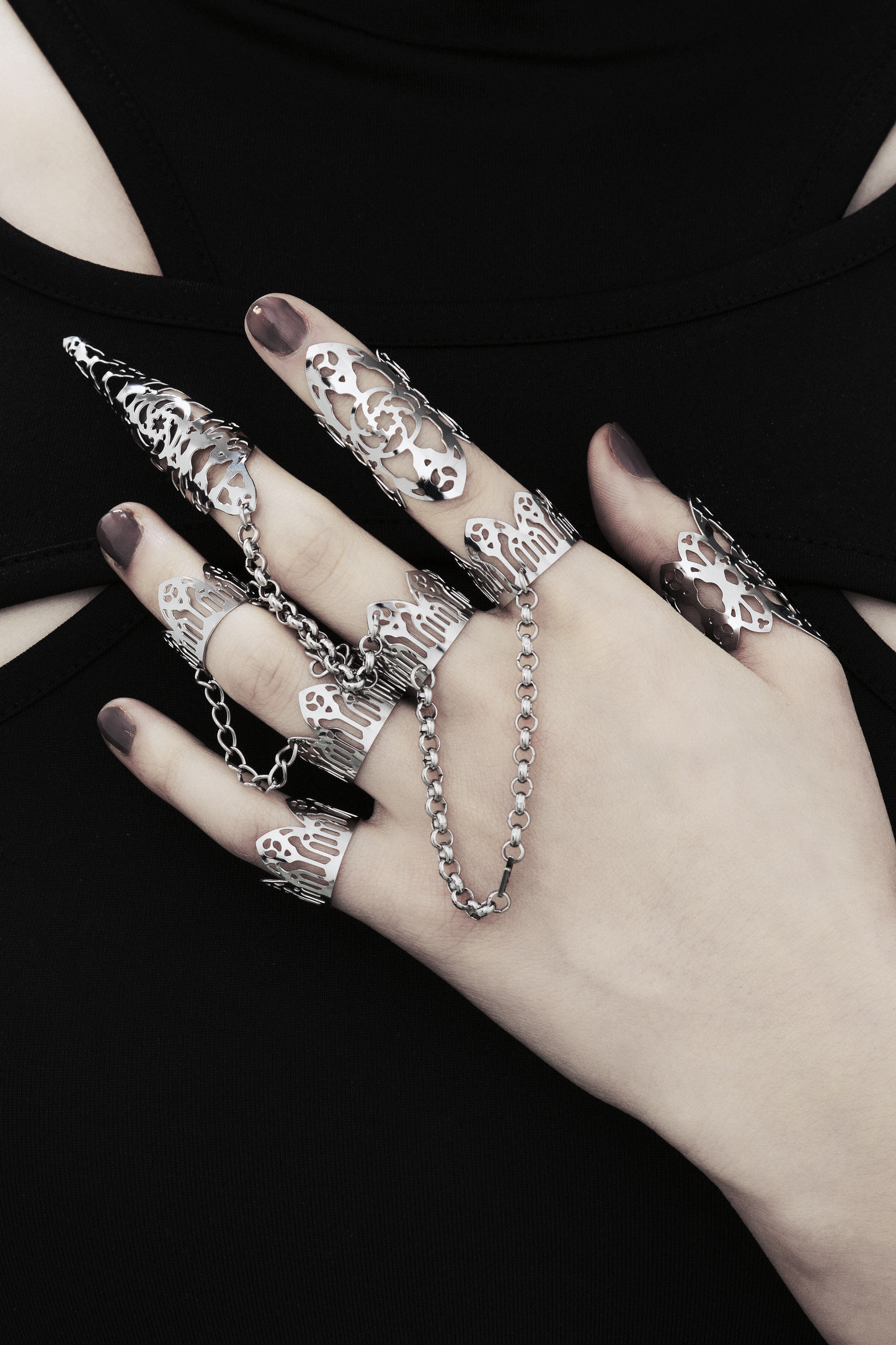 A display of Myril Jewels' handcrafted, dark-avantgarde rings on a hand, each with intricate gothic-inspired designs, ideal for aficionados of alternative and gothic styles. The rings range from slim bands to dramatic, extended pieces resembling talons, all connected by slender chains, presenting a statement of bold elegance. These Italian-made pieces embody the unique, evolving aesthetic of Myril Jewels, tailored for the discerning tastes of the gothic jewelry enthusiast.