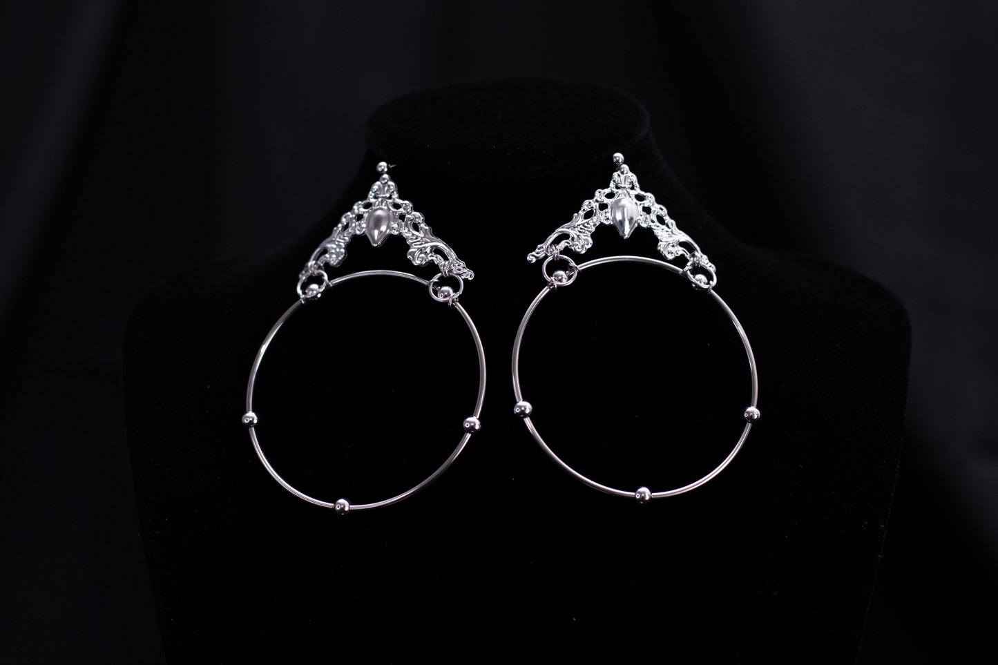 A pair of Myril Jewels' bold gothic hoop earrings featuring an expansive design and ornate details. These hoops combine classic elegance with neo-gothic flair, making them an ideal gift for those who love a statement piece. Their unique style suits various occasions, from Halloween to everyday wear, reflecting the dark, avant-garde aesthetic of the Myril Jewels brand.