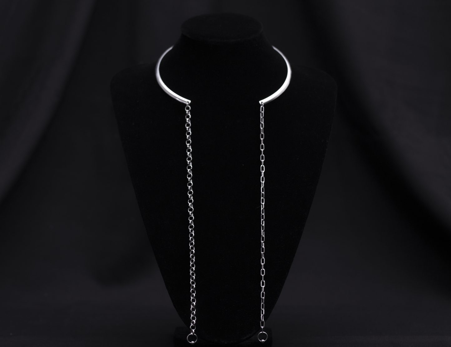  A sleek and minimal Myril Jewels necklace features a rigid, crescent-shaped neckline with long, delicate chains draping elegantly on a black velvet mannequin. This piece embodies the subtle edge of neo-gothic design, making it versatile for Witchcore enthusiasts, Halloween adornment, or as a sophisticated everyday accessory.