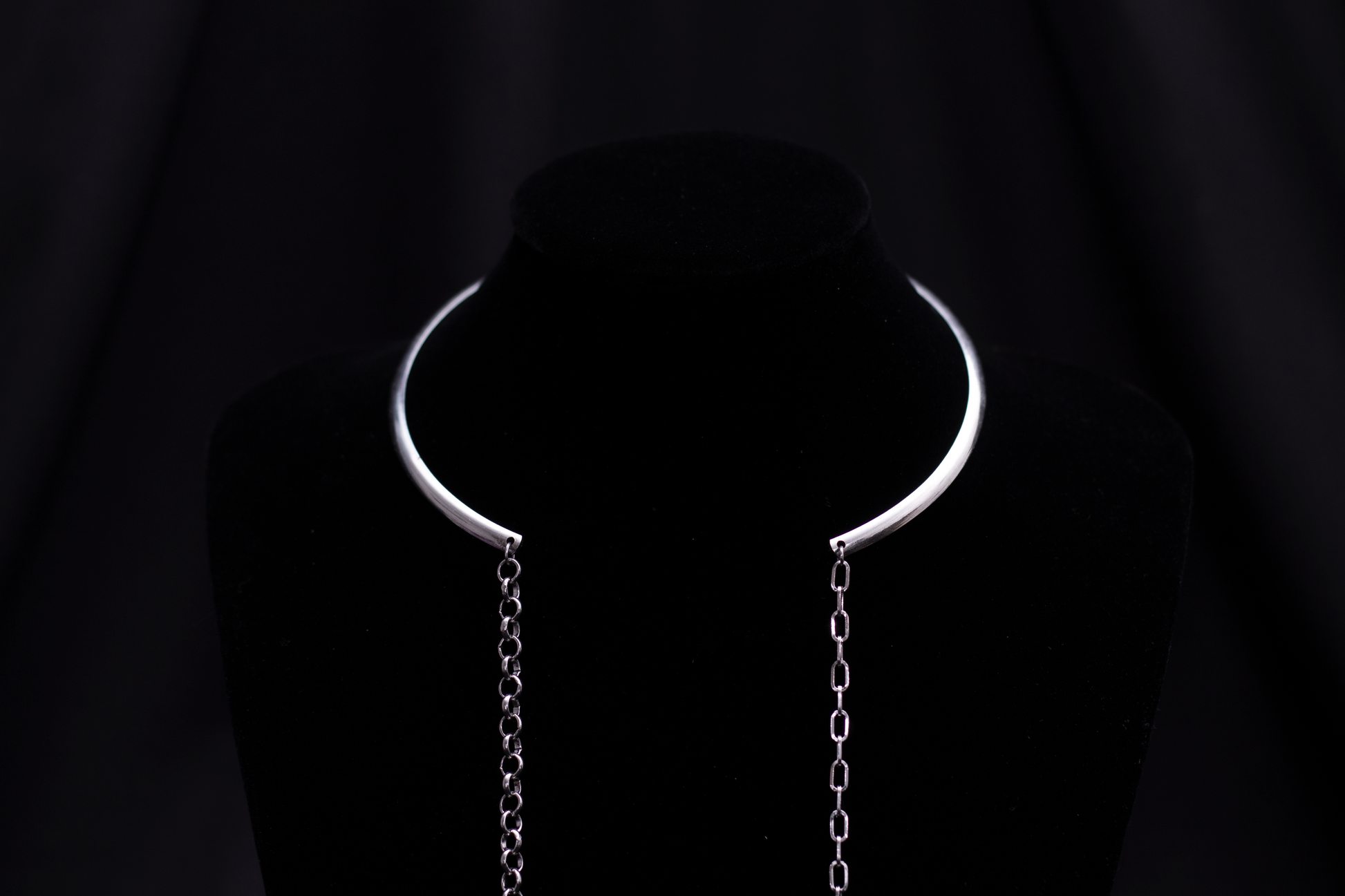 Displayed on a black mannequin, a Myril Jewels rigid minimal necklace with two long hanging chains creates a stark, elegant silhouette. This piece is emblematic of the brand's dark-avantgarde aesthetic, suited for gothic, whimsigoth, and minimal goth styles, making it a versatile accessory for everyday wear or special events like festivals.