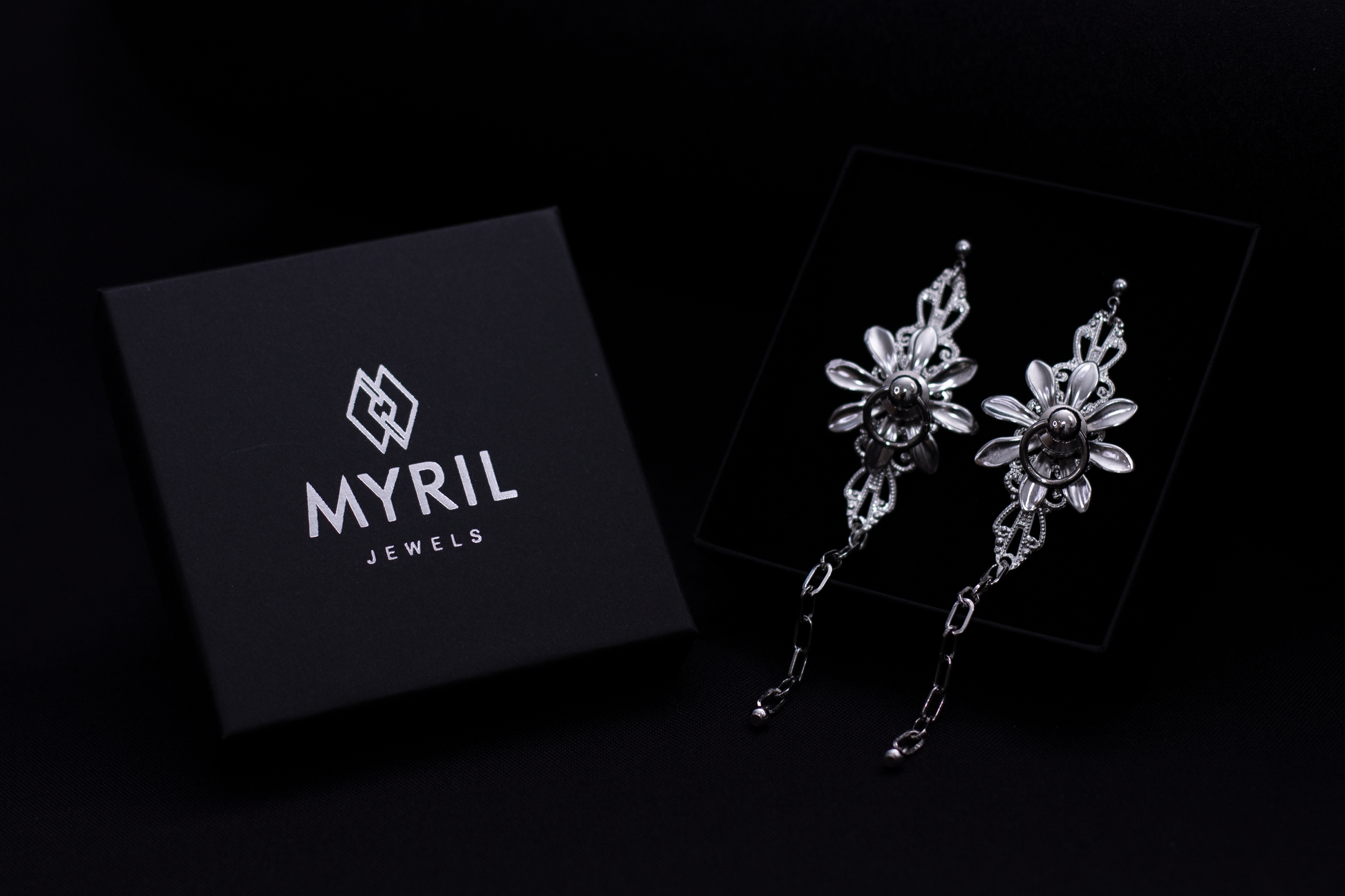 Neo-gothic floral earrings by Myril Jewels rest elegantly in their sleek packaging, radiating dark avant-garde allure. These bold, handmade pieces feature intricate petals and a dramatic hanging chain, perfect for gothic-chic enthusiasts or as a statement Halloween or festival jewel. Ideal for goth girlfriend or friend gifts, they epitomize minimalist goth elegance for everyday wear or rave parties.