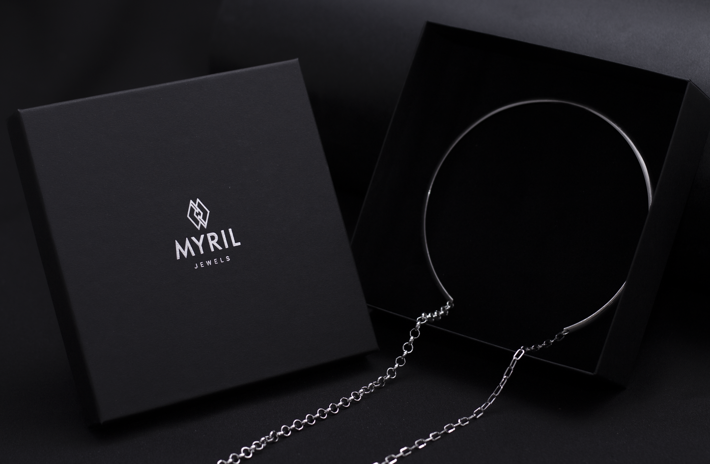 Elegant Myril Jewels packaging presents a sleek, rigid necklace with long hanging chains, reflecting a minimalist neo-goth style for the modern, dark-avantgarde enthusiast.