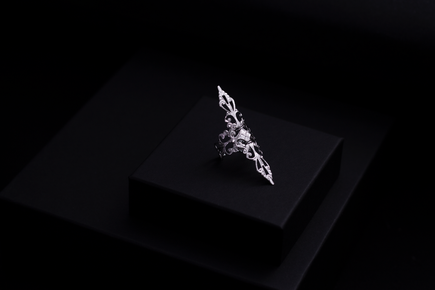 A sleek Myril Jewels' ring on a dark surface, revealing a sophisticated silver filigree expressing the brand's refined gothic jewelry collection.