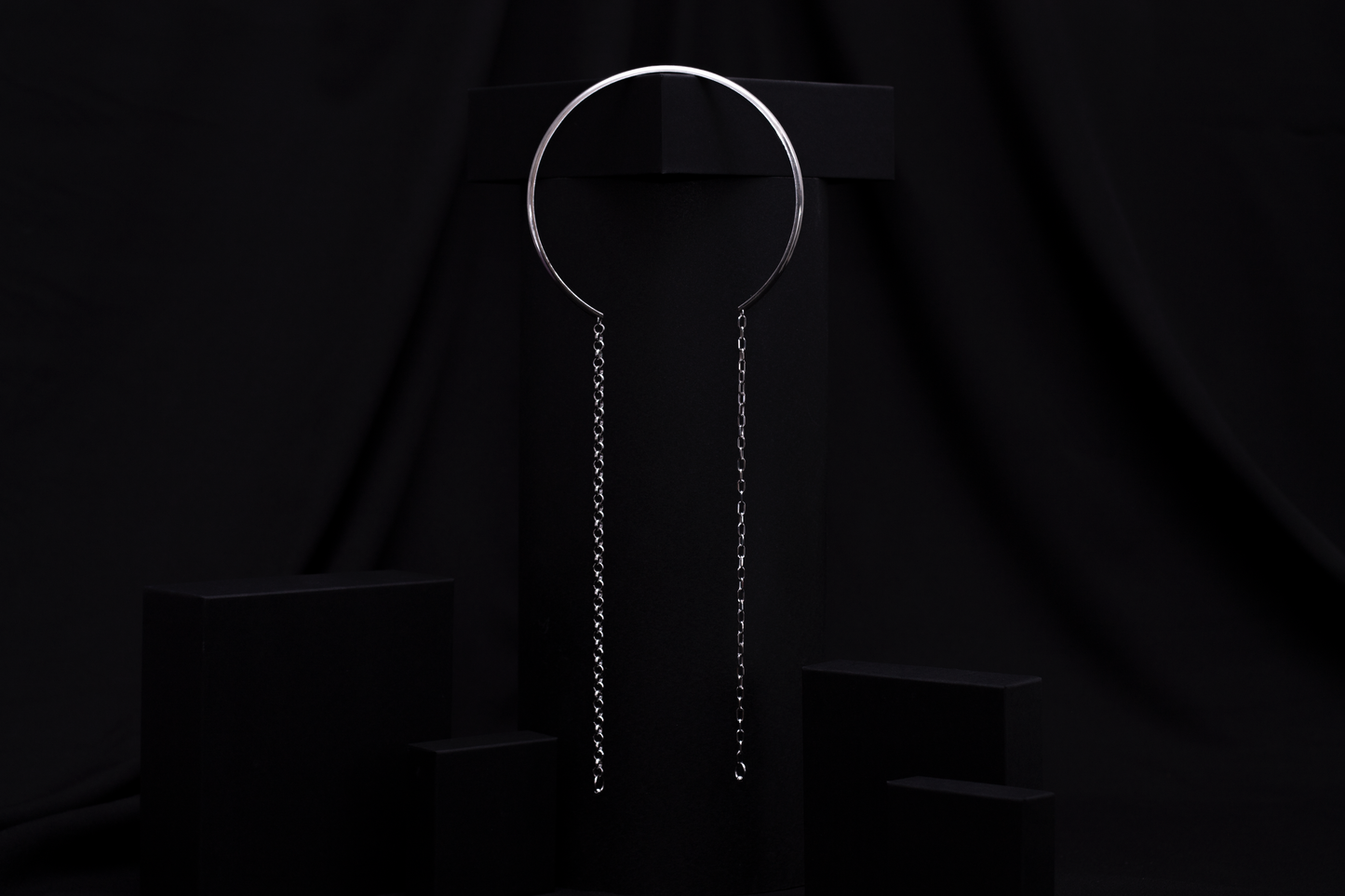 Displayed against a black backdrop, this Myril Jewels piece features a rigid, minimal necklace with long hanging chains, encapsulating the essence of minimal goth. This refined item is ideal for adding an avant-garde touch to any outfit, suitable for everyday wear or as a distinctive accessory for special events like festivals.