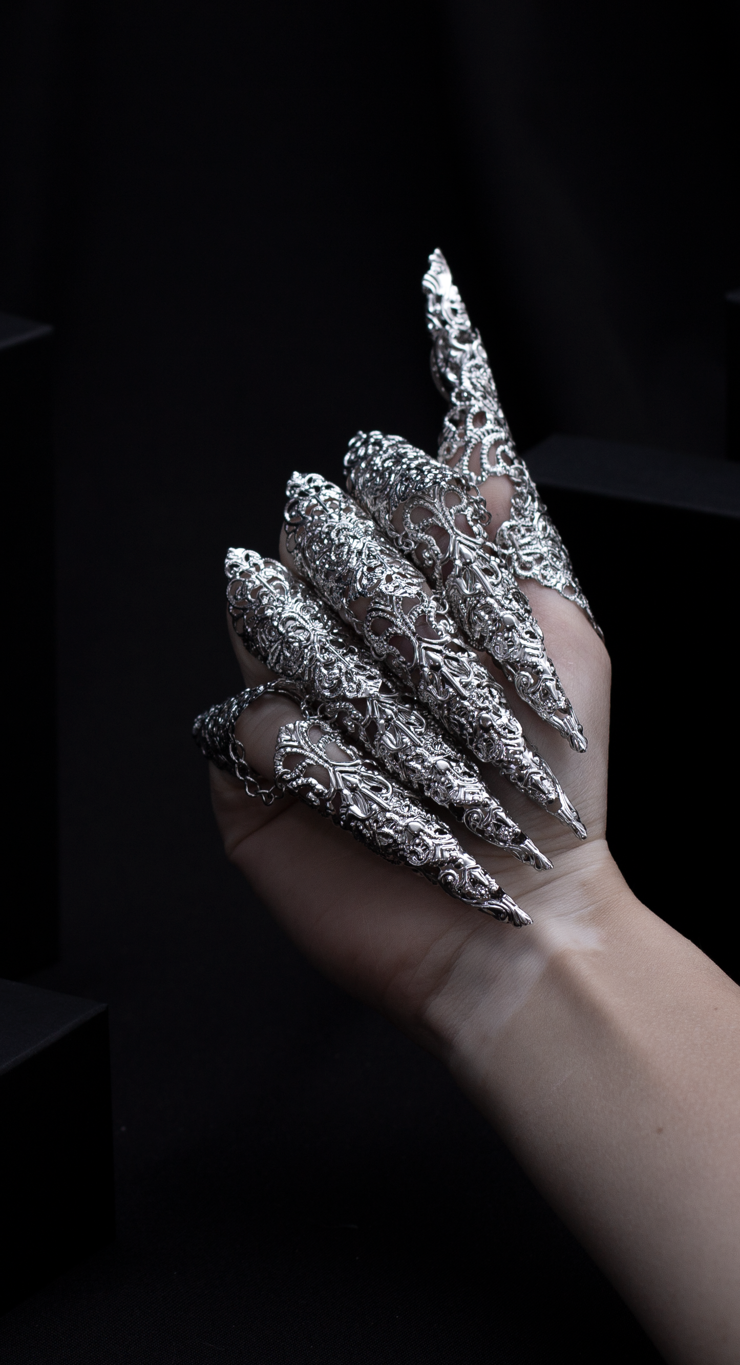 "A hand emerges from the shadows, flaunting Myril Jewels' midi rings with striking long claws, a perfect blend of neo-gothic flair and dark avant-garde elegance. This bold jewelry makes an ideal statement for Halloween, adding a touch of gothic-chic to any outfit.