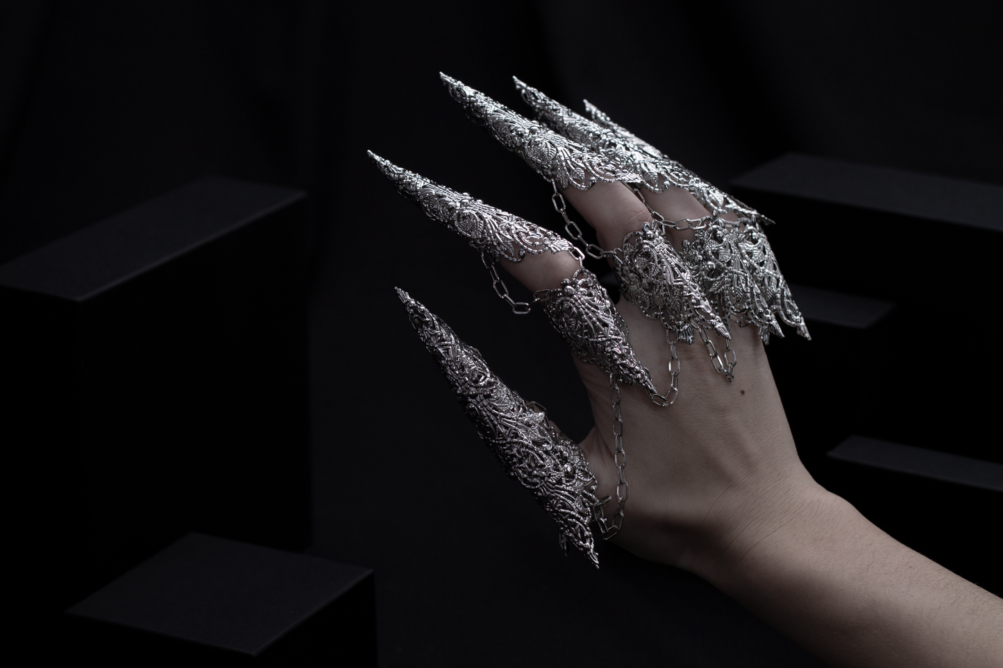 A hand is strikingly adorned with a set of Myril Jewels' dragon-like long claw rings, casting a neo-gothic spell. This bold jewelry, embodying the essence of dark avant-garde, is a dream for gothic style enthusiasts, making it an ideal choice for Halloween or as a unique gift.