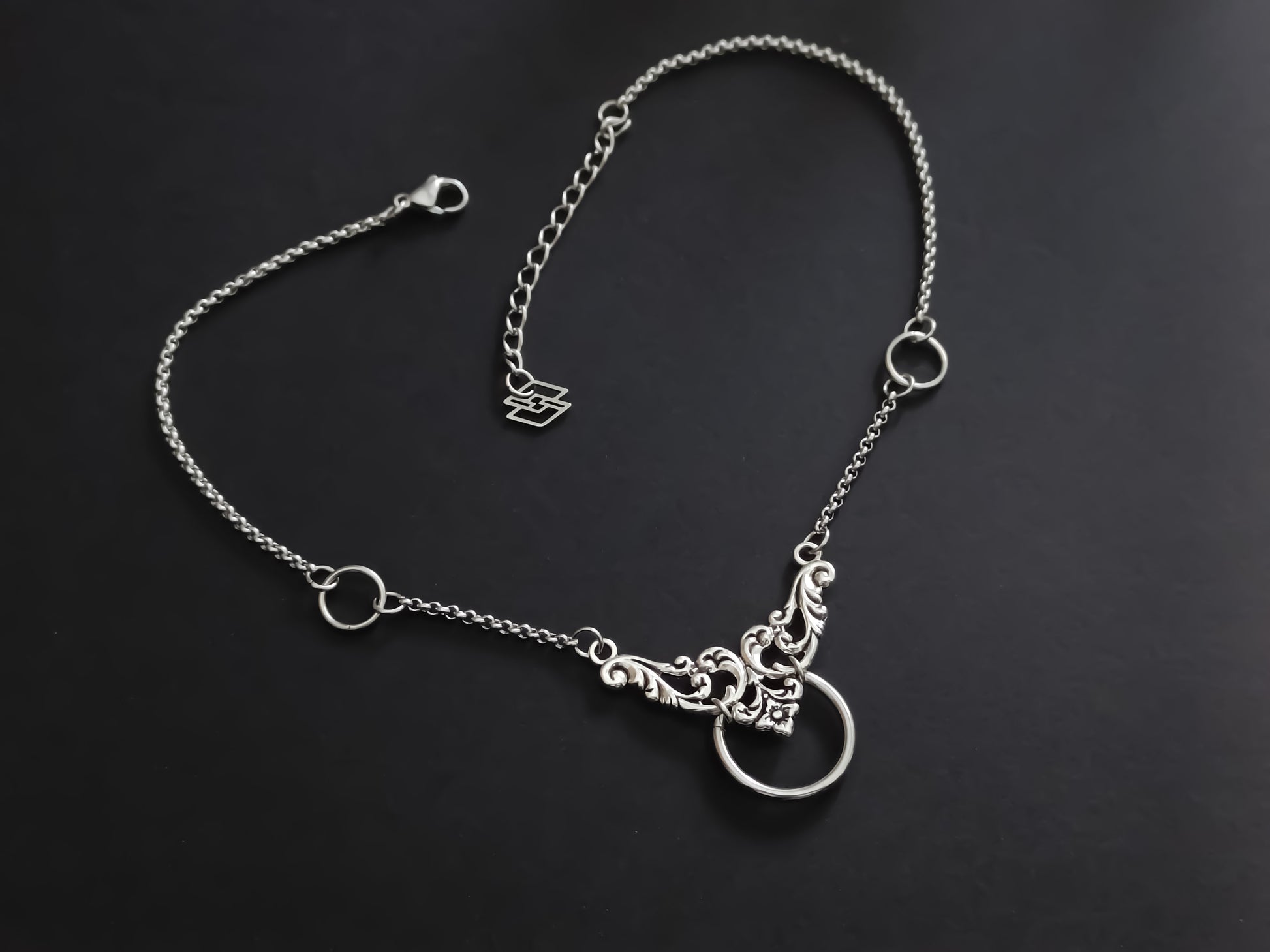 This image displays a Myril Jewels elegant chain choker, featuring a floral motif and central O-ring, embodying the sophisticated, dark-avantgarde aesthetic of neo-goth style.