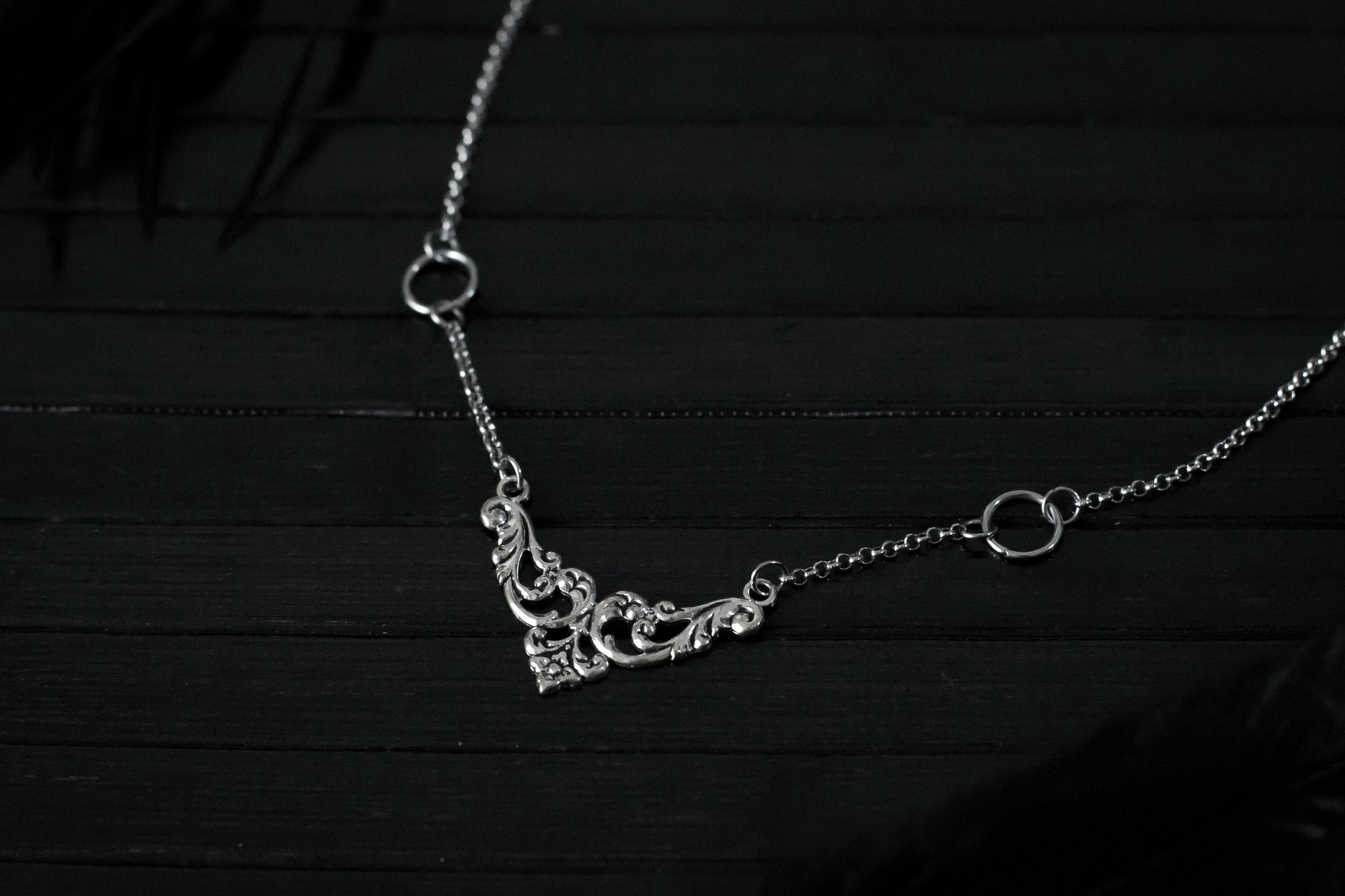 Displayed on a black layer is a Myril Jewels elegant gothic necklace, capturing the essence of neo-goth fashion. The necklace, with a fine silver chain, features ornate filigree detailing and symmetrical O-ring accents, embodying the dark-avantgarde aesthetic. This piece is designed for gothic and alternative style aficionados, seamlessly blending with Halloween, punk, and gothic-chic ensembles, and is a sophisticated choice for whimsigoth, witchcore, or minimal goth everyday wear