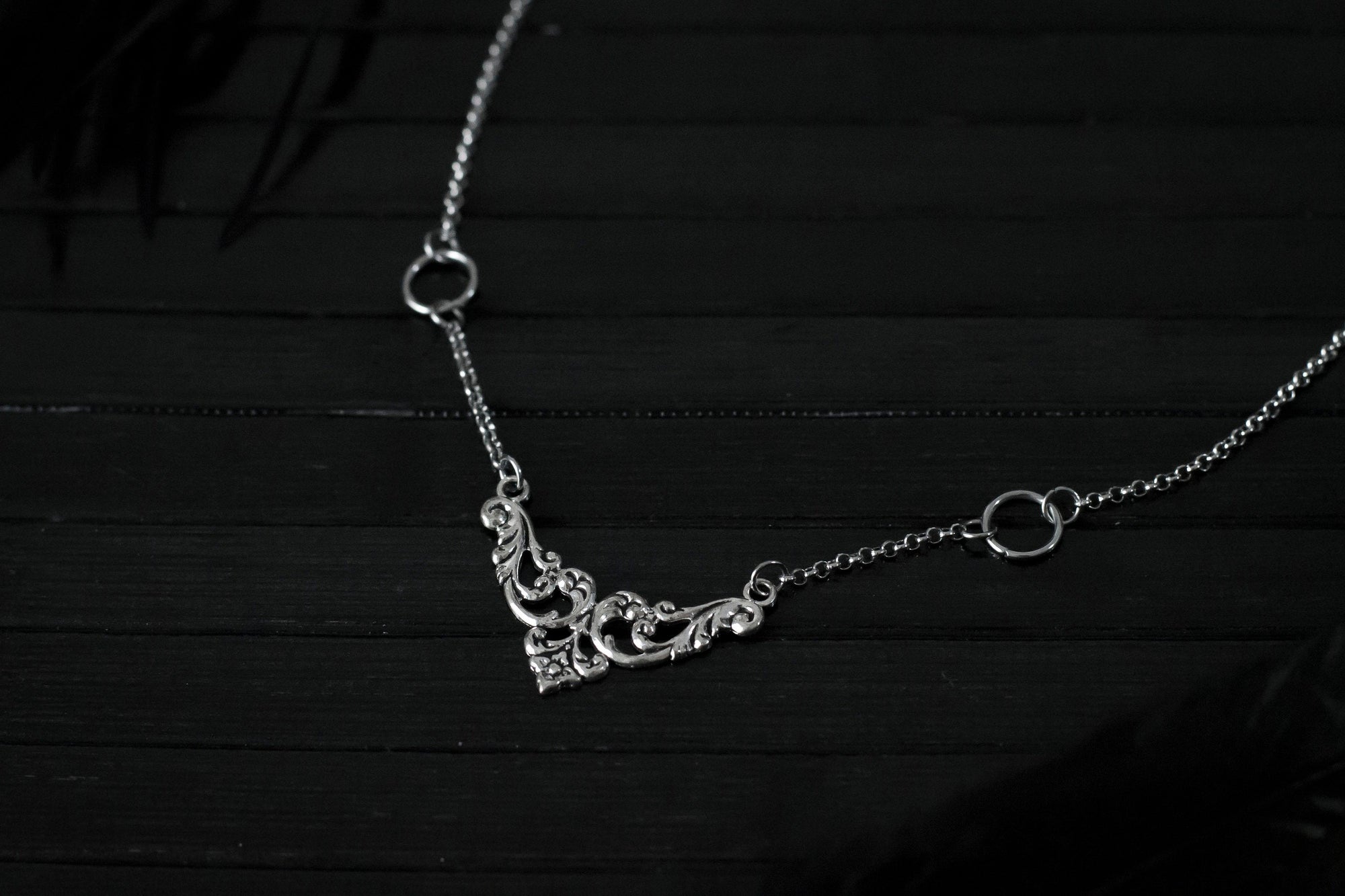 Displayed on a black layer is a Myril Jewels elegant gothic necklace, capturing the essence of neo-goth fashion. The necklace, with a fine silver chain, features ornate filigree detailing and symmetrical O-ring accents, embodying the dark-avantgarde aesthetic. This piece is designed for gothic and alternative style aficionados, seamlessly blending with Halloween, punk, and gothic-chic ensembles, and is a sophisticated choice for whimsigoth, witchcore, or minimal goth everyday wear