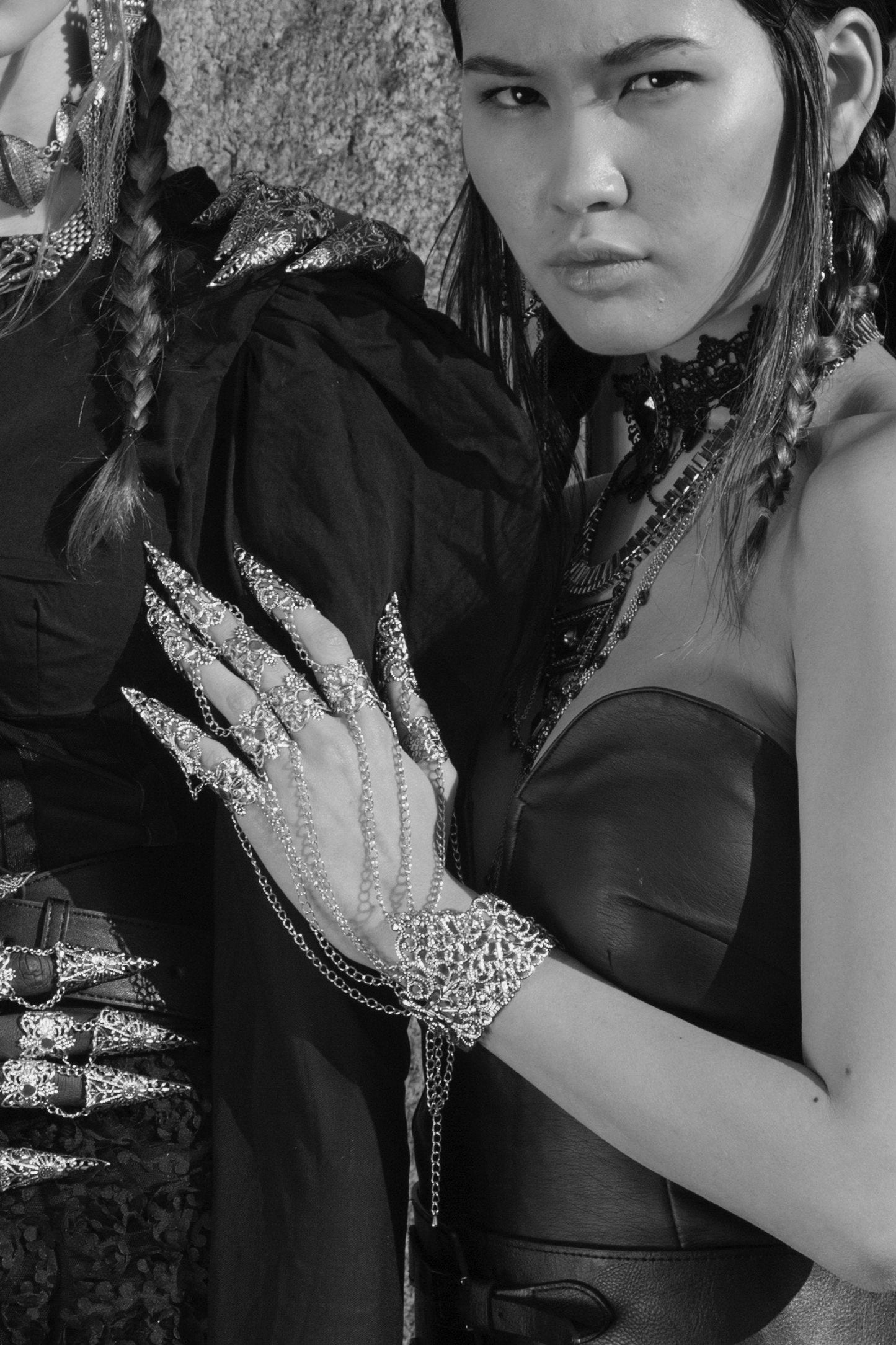 A black and white photograph showcases a fashion model in a dynamic pose, her hand adorned with a Myril Jewels metal glove with striking finger claw rings. The glove's detailed design echoes the neo-goth aesthetic, a perfect statement piece for gothic, punk, and alternative styles.