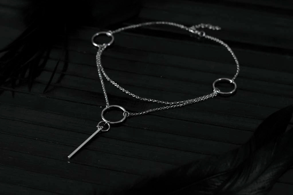 A sleek Myril Jewels minimal chain necklace with hoops, displayed on a black mannequin, encapsulates the essence of dark-avantgarde style for the modern gothic enthusiast.