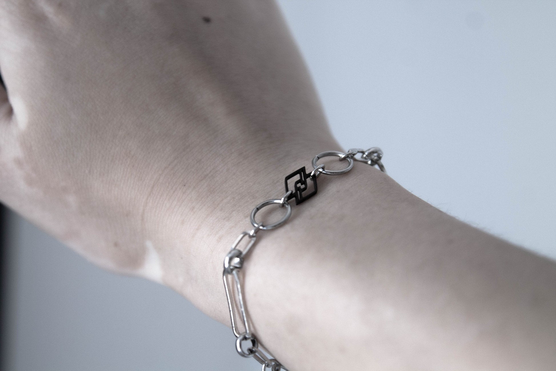 A model showcases a Myril Jewels chain bracelet, embodying the essence of dark avant-garde with a touch of everyday minimal goth. This handcrafted piece reflects the brand's commitment to sophisticated, futuristic designs for those who revel in gothic, witchcore, and whimsigoth styles. The bracelet's silver-toned links catch the light, complementing the model's striking black nail polish, making it a perfect accessory for both Halloween festivities and neo-gothic everyday fashion.