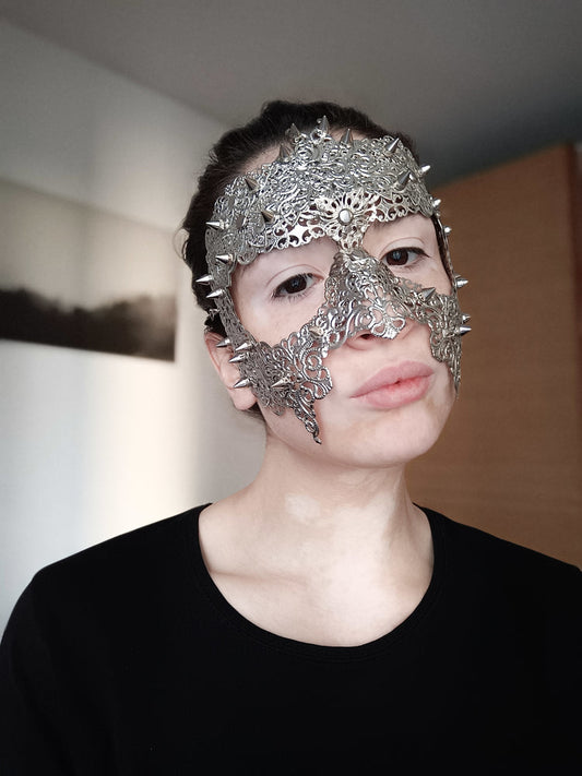  A model dons a Myril Jewels full-face filigree mask with studs, a punk-inspired piece for gothic and alternative style lovers. Ideal for dramatic flair at Halloween, festivals, or as a bold statement accessory, perfect for adding dark-avantgarde sophistication to any outfit.