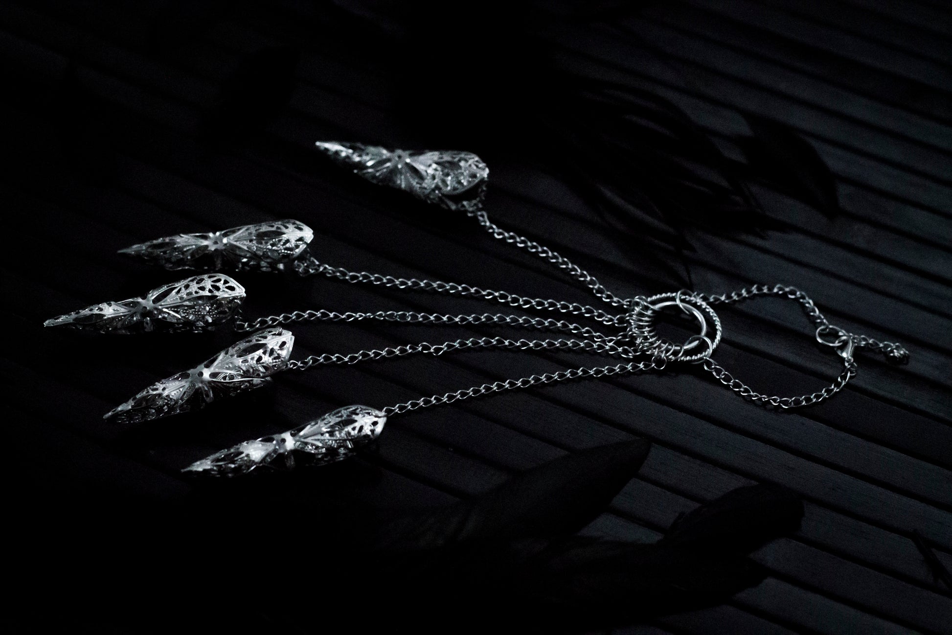 A close up shoot of a hand that extends dramatically with Myril Jewels' hand chain bracelet, each finger tipped with a delicate claw ring. The jewelry's silver filigree work captures the dark, neo-gothic aesthetic, perfect for adding a bold touch to Halloween looks or as a statement piece for those who favor gothic-chic or witchcore styles.
