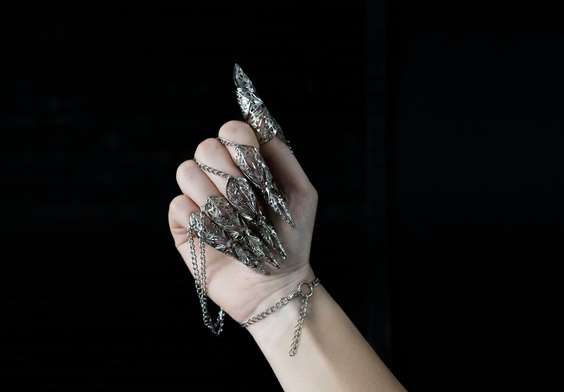 A hand adorned with Myril Jewels' hand chain bracelet with silver claws, reflecting a darkly opulent neo-goth style. This captivating piece is perfect for those who favor gothic-chic jewelry, making it an ideal choice for witchcore looks, rave parties, or as a daring gift for the bold at heart.