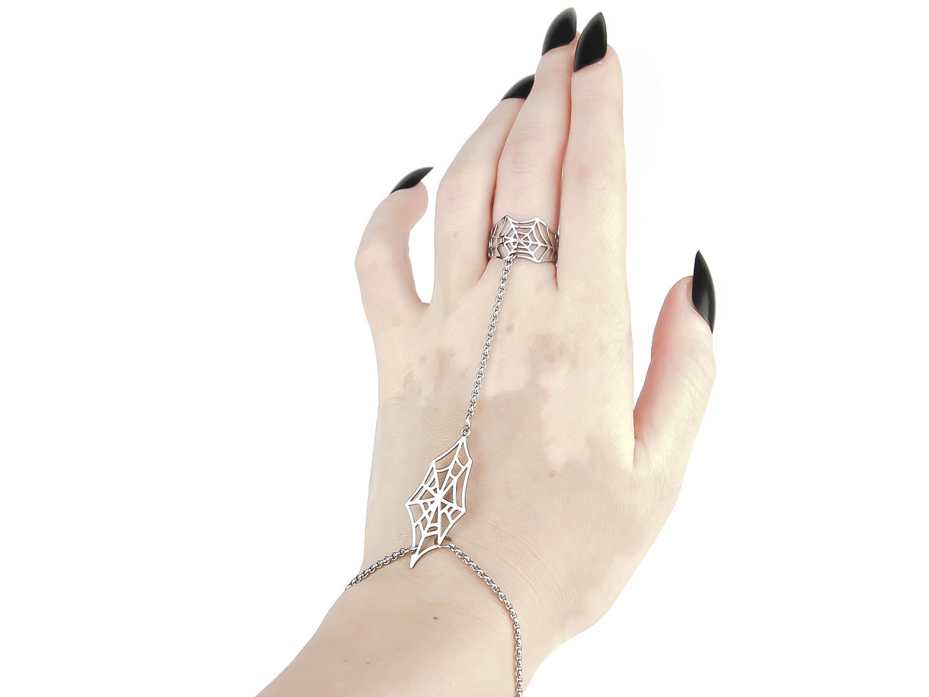A graceful hand chain bracelet ring from Myril Jewels, designed with a spiderweb motif, adorns the wrist and finger of a hand with polished black nails. This neo-goth jewelry piece is a fusion of dark-avantgarde elegance and gothic-chic, perfect for Halloween and everyday wear. The silver spiderweb design bridges the gap between punk jewelry and whimsigoth aesthetics, making it a versatile accessory for witchcore followers or as a distinctive touch to rave party and festival outfits