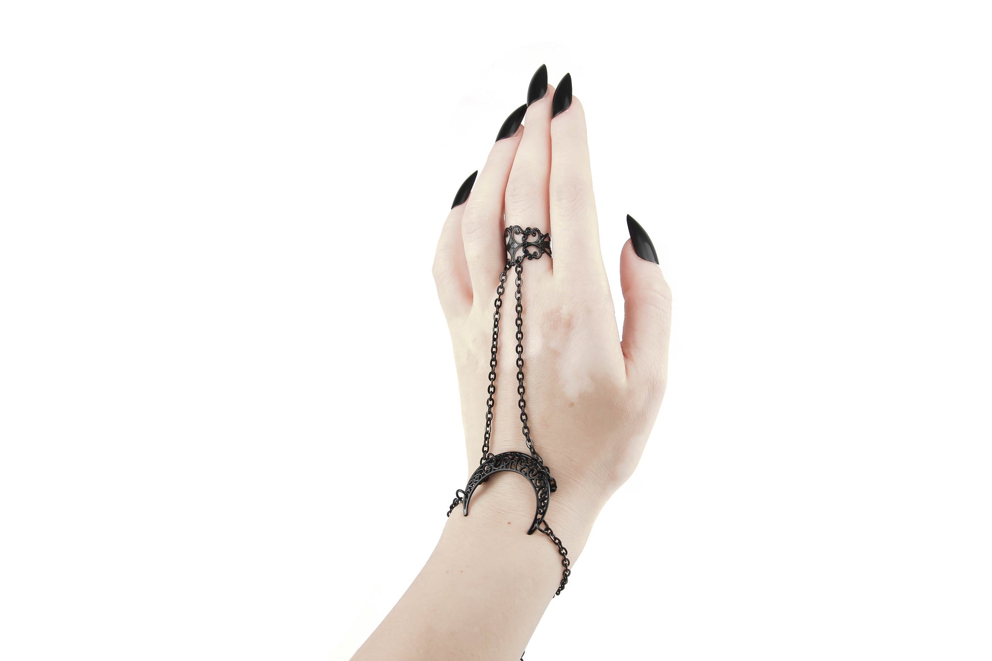 A hand is gracefully displayed with a Myril Jewels black hand chain, featuring a moon-shaped bracelet and a delicate chain that connects to a ring. This piece embodies the dark-avantgarde essence of Myril Jewels, perfect for gothic style enthusiasts looking to add a celestial touch to their wardrobe, suitable for everyday wear or as a statement piece for special occasions.