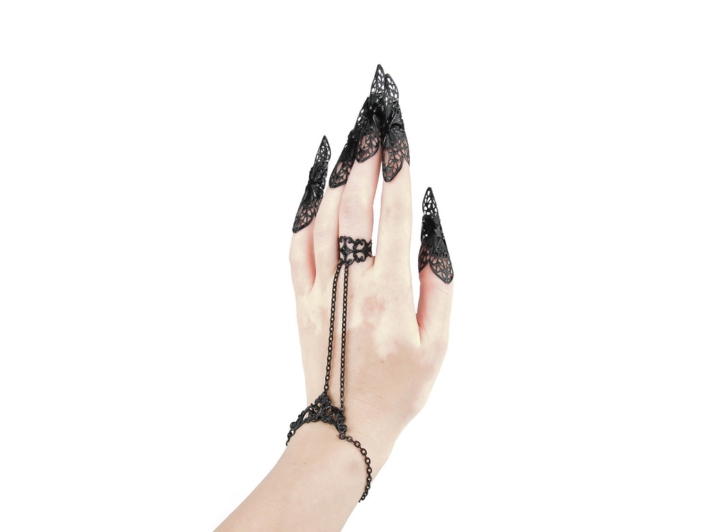 A striking Myril Jewels hand chain bracelet ring cascades from a baroque filigree ring down to a matching wrist adornment, paired with long, ornate nail claw rings. This dark, avant-garde set is a masterpiece of gothic chic, ideal for those who adore Halloween jewelry, Punk aesthetics, and Neo Gothic finery. Each intricate claw ring is a testament to the artistry that caters to the whims of Witchcore enthusiasts and festival-goers seeking minimal goth elegance