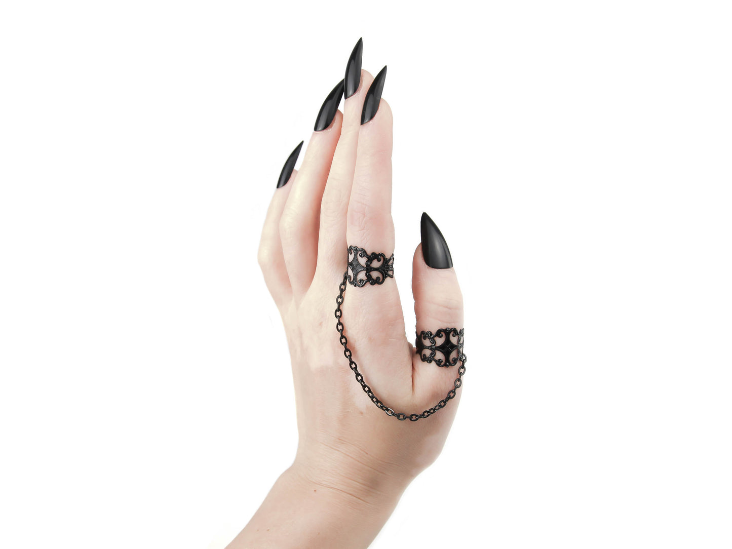 A hand with sleek black nails presents Myril Jewels' ornate black rings, connected by a fine chain, embodying the dark-avantgarde spirit. Perfect for gothic-chic, punk, or whimsigoth aesthetics, these rings are a must-have for any alternative style, especially during Halloween and neo-gothic events.