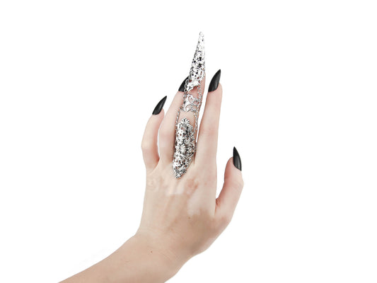 A hand models on the middle finger a striking Myril Jewels articulated finger armor ring, with polished silver filigree detailing perfect for dark-avantgarde and gothic fashion enthusiasts. This Italian-made, handcrafted piece captures the essence of alternative luxury.