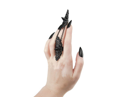 Presented is an elegant Myril Jewels studded claw ring in black, gracing the middle finger with its ornate filigree design. This distinctive piece epitomizes neo-goth jewelry, a perfect blend of punk edge and gothic-chic sophistication. It's an ideal choice for those who favor dark-avantgarde accessories, seamlessly fitting for Halloween, everyday witchcore style, or as an eye-catching complement to rave party and festival attire.