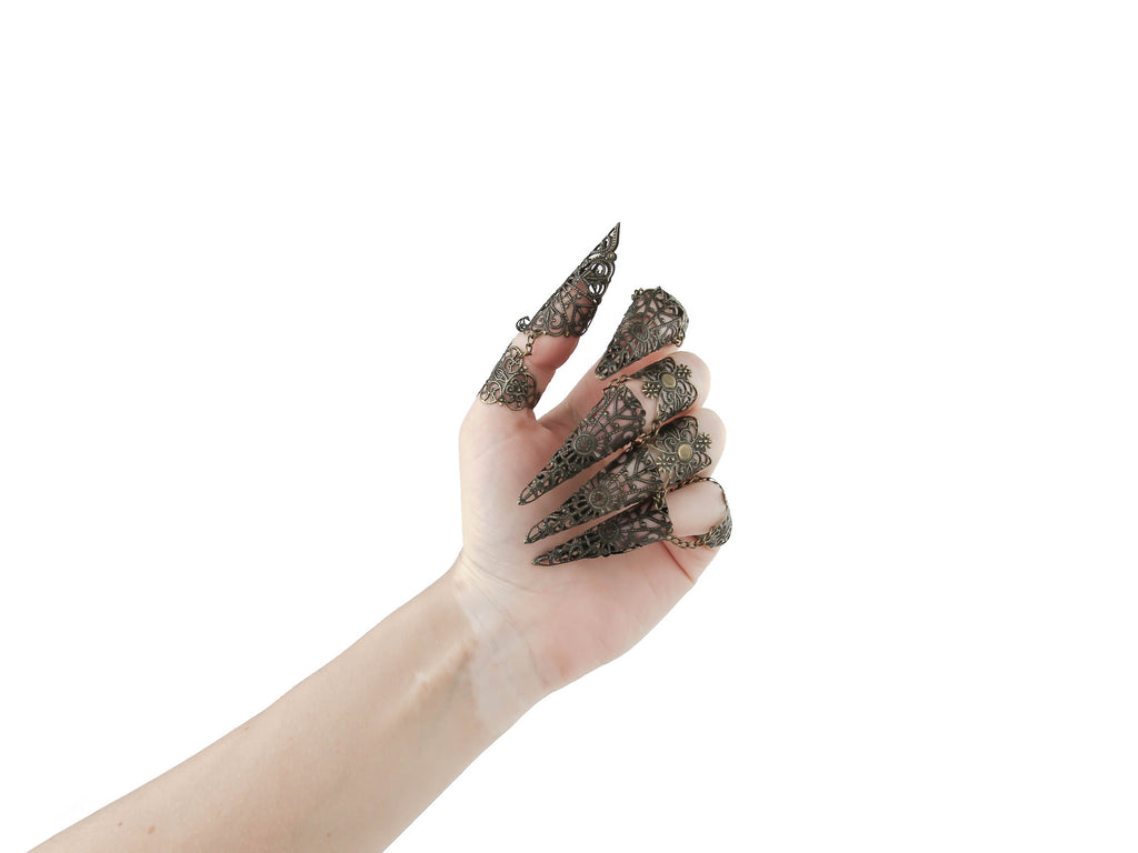 Showcase the striking allure of Myril Jewels with this full hand set of bronze midi rings, each ring extending into an elegant claw design. The intricate detail reflects a neo-gothic aesthetic, perfect for the gothic and alternative style connoisseur. These rings are an impeccable choice for Halloween, embodying the essence of punk jewelry and witchcore. They serve as an avant-garde statement piece, ideal for minimal goth everyday wear or as a dramatic accessory for rave parties and festivals