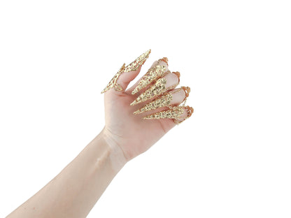 A hand is adorned with a striking set of gold claw rings from Myril Jewels, featuring detailed neo-gothic designs perfect for individuals who embrace gothic and alternative styles. These claw rings serve as an eye-catching addition for Halloween, complementing punk and gothic-chic wardrobes, and add an edgy touch to minimal goth or witchcore daily attire. They are also ideal for enhancing rave party outfits, festival looks, or as a unique gift for a goth girlfriend.