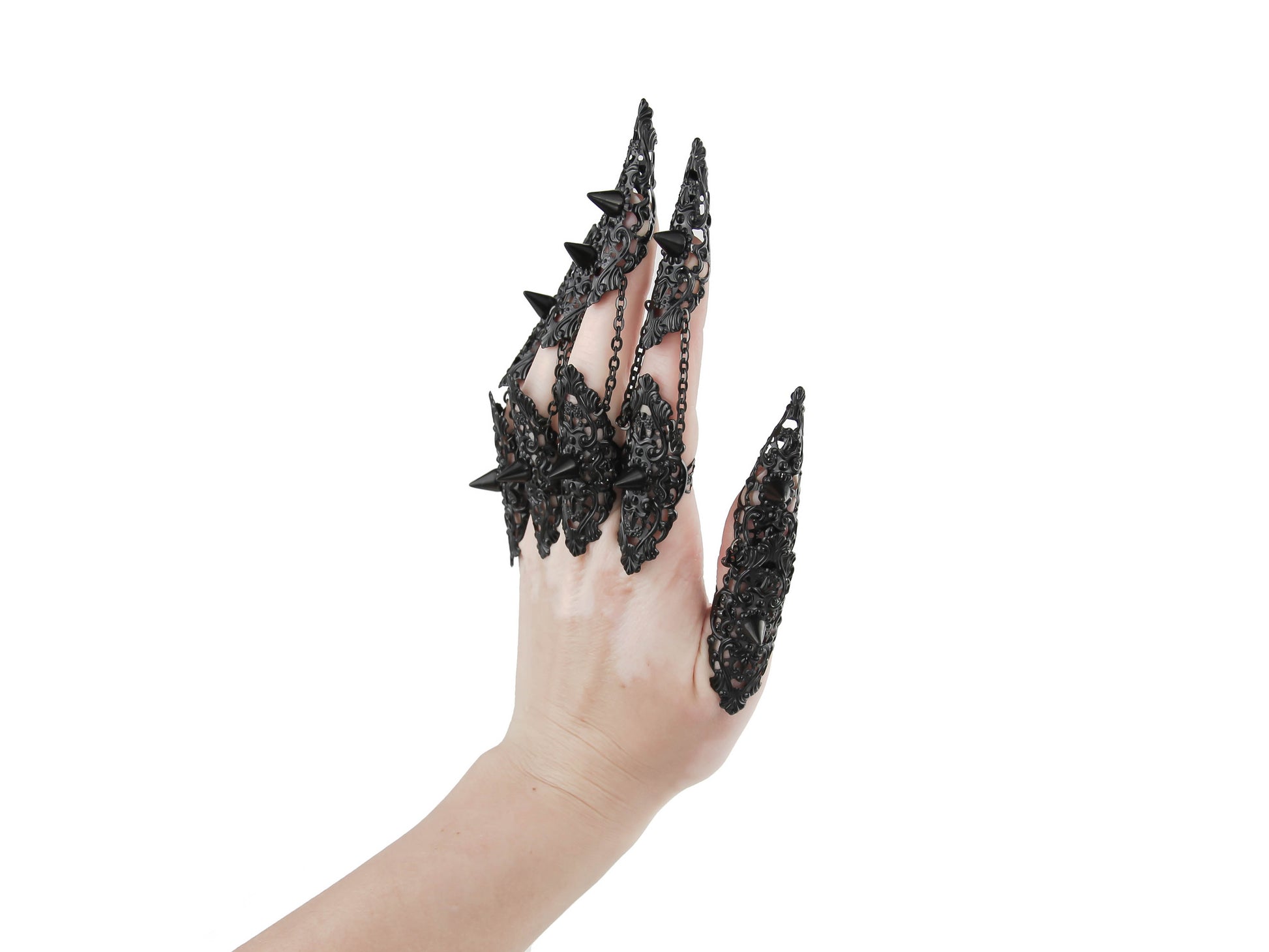 A hand is dramatically extended, displaying a full set of Myril Jewels studded nail claw rings in black. Each claw ring is elaborately designed with spikes and filigree, reflecting a dark-avantgarde and neo-goth aesthetic. These bold pieces are tailored for gothic, punk, and alternative style enthusiasts, perfect for Halloween, and suitable as an expressive accessory for everyday wear. They embody the gothic-chic look, enhancing whimsigoth and witchcore outfits, and making a statement at rave parties