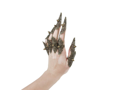 A hand is dramatically adorned with a full set of Myril Jewels studded nail claw rings in bronze. The claw rings feature elaborate filigree with pointed studs, invoking a bold neo-goth aesthetic. These edgy, dark-avantgarde pieces are perfect for those who embrace gothic and alternative styles, making them an ideal choice for Halloween, punk-inspired outfits, or as a statement addition to a whimsigoth or witchcore look. They also serve as eye-catching accessories for minimal goth everyday wear