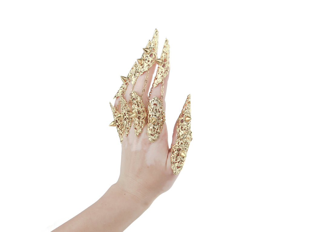 An image captures a hand fully clad in Myril Jewels' studded gold nail claw rings, each piece boasting intricate detailing and sharp studs that epitomize the neo-goth aesthetic. This daring collection is ideal for those who embrace the dark-avantgarde culture, perfect as an edgy accessory for Halloween, punk events, or to add a gothic-chic flair to everyday attire. These rings are a bold statement for witchcore, whimsigoth, or minimal goth styles and will turn heads at any rave party or festival.