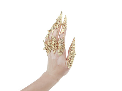 An image captures a hand fully clad in Myril Jewels' studded gold nail claw rings, each piece boasting intricate detailing and sharp studs that epitomize the neo-goth aesthetic. This daring collection is ideal for those who embrace the dark-avantgarde culture, perfect as an edgy accessory for Halloween, punk events, or to add a gothic-chic flair to everyday attire. These rings are a bold statement for witchcore, whimsigoth, or minimal goth styles and will turn heads at any rave party or festival.