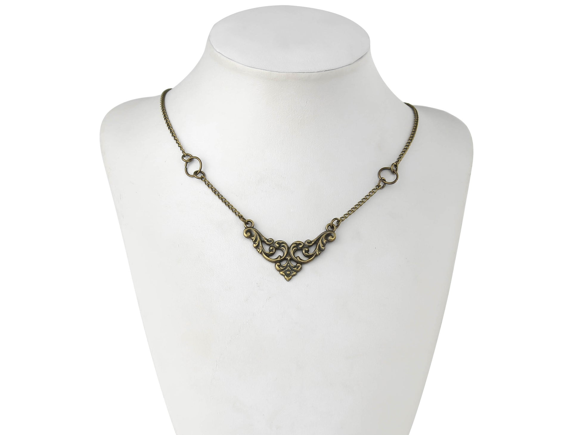 A delicate gothic necklace by Myril Jewels is displayed on a mannequin, featuring fine bronze detailing that captures the essence of neo-gothic design. The bronze necklace showcases intricate filigree work, forming a symmetrical, ornamental centerpiece, flanked by two simple loops, embodying a blend of gothic-chic and minimalist aesthetics. This piece is ideal for those who appreciate dark-avantgarde jewelry, suitable for witchcore, everyday wear, or as a subtle complement to rave party and festival outfits