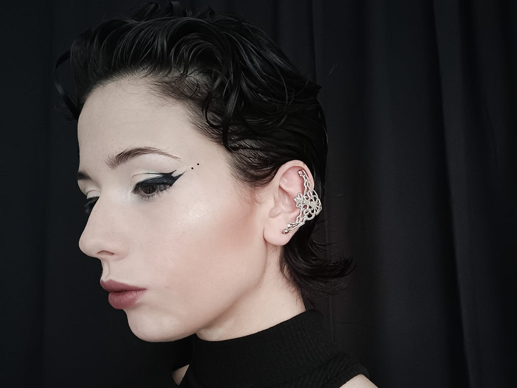 A profile view of a model wearing Myril Jewels cuff earrings, showcasing a neo-goth design with intricate filigree details. The earrings, resembling elegant gothic arches, complement the model's dark avant-garde style. This gothic-chic accessory is perfect for those embracing a whimsigoth or witchcore aesthetic, versatile enough for everyday wear, and striking for a Halloween or festival ensemble. The model's sleek hairstyle and bold eyeliner accentuate the earrings