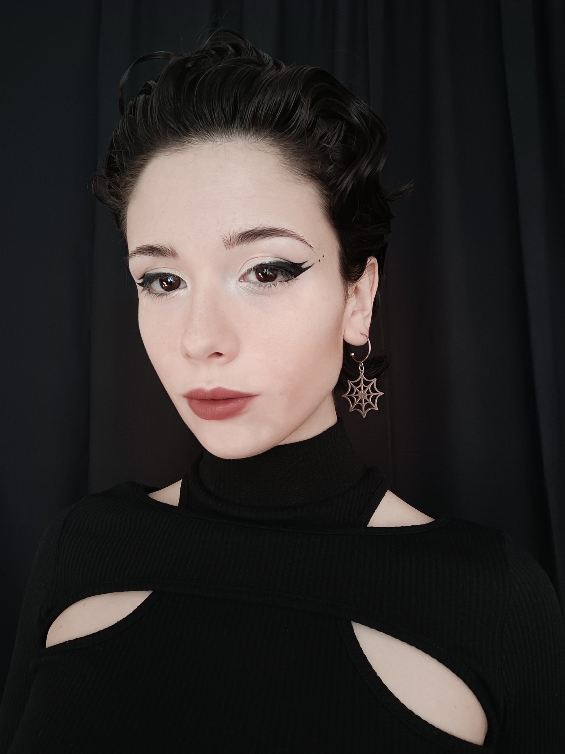 A poised model showcases Myril Jewels' half hoop spiderweb earrings, embodying a dark avant-garde aesthetic. These intricate earrings, perfect for gothic and alternative fashion enthusiasts, add a touch of neo-gothic charm to any outfit, suitable for everyday wear, Halloween, or whimsigoth styles.
