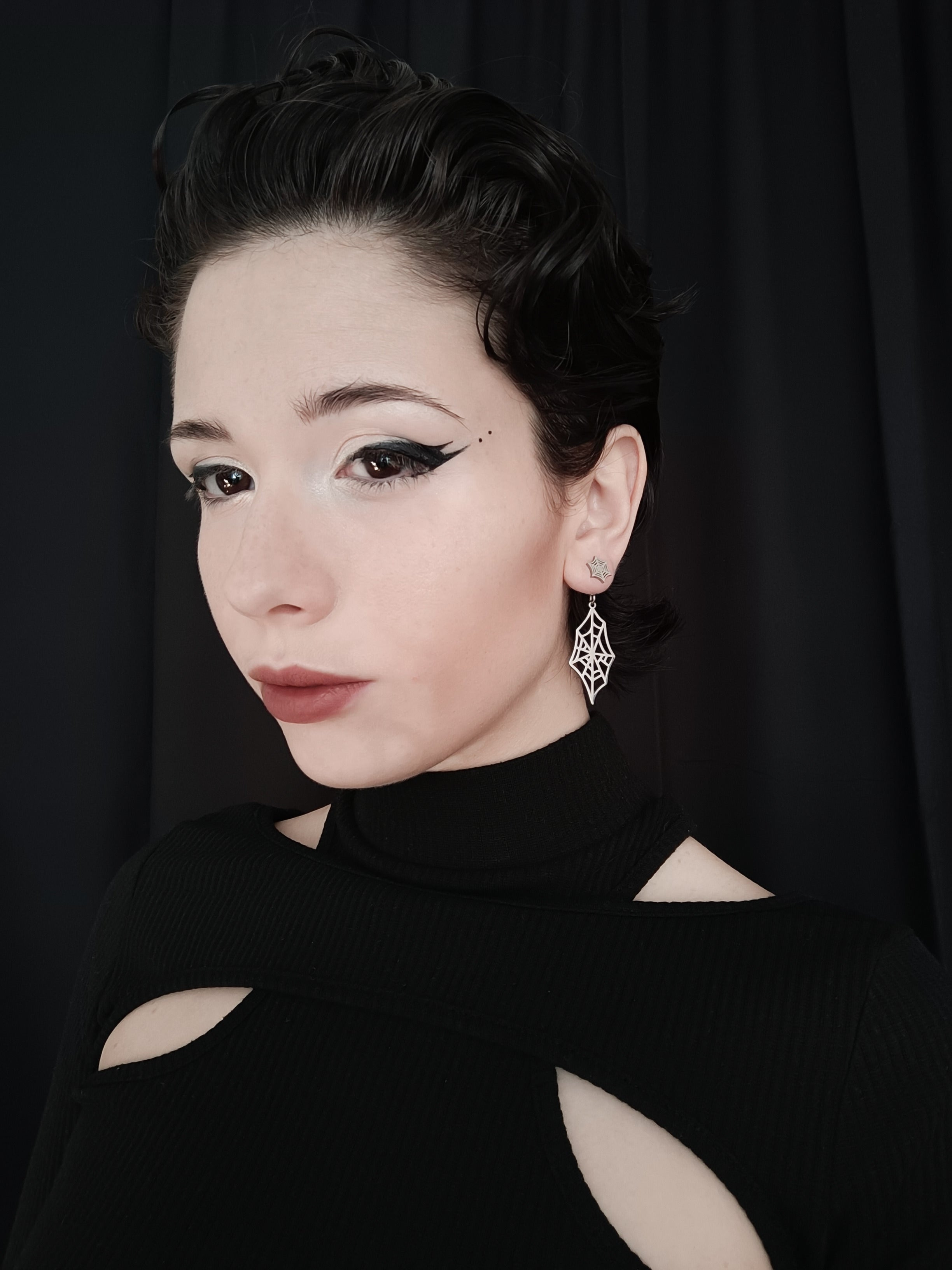 A model exudes gothic elegance with Myril Jewels' spiderweb earrings, a quintessential piece for lovers of neo-goth jewelry. These finely crafted earrings, with their intricate web-like design, are a testament to dark-avantgarde artistry, perfect for adding a touch of gothic-chic to any ensemble. The earrings are showcased against a sleek black outfit, making them ideal for everyday wear, Halloween adornment, or as a distinctive accessory for rave parties and festivals