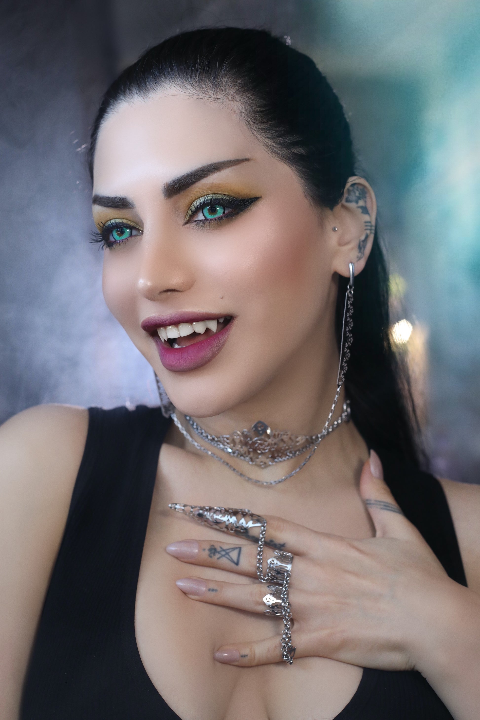A woman models Myril Jewels' sophisticated handcrafted jewelry: a dramatic double ring connected by a slender chain, featuring claw-like detailing and gothic arch patterns, and intricate filigree work that echoes neo-gothic design. The ensemble is completed with matching elaborate earrings and multi-layered necklaces, which encapsulate the brand’s dark-avantgarde aesthetic, perfect for gothic and alternative fashion aficionados seeking bold and unique accessories.