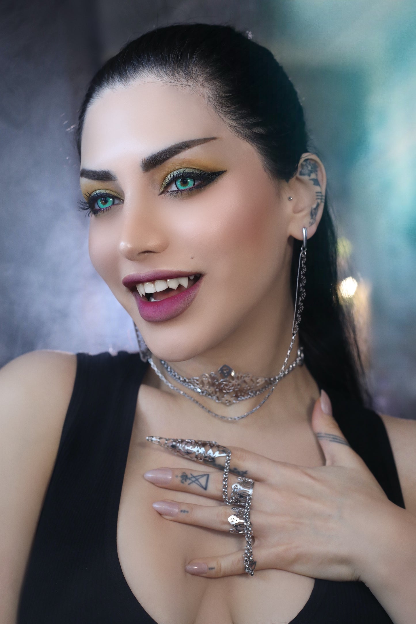 A woman models Myril Jewels' sophisticated handcrafted jewelry: a dramatic double ring connected by a slender chain, featuring claw-like detailing and gothic arch patterns, and intricate filigree work that echoes neo-gothic design. The ensemble is completed with matching elaborate earrings and multi-layered necklaces, which encapsulate the brand’s dark-avantgarde aesthetic, perfect for gothic and alternative fashion aficionados seeking bold and unique accessories.
